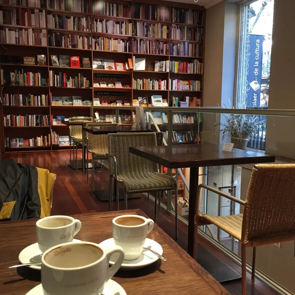 Interior de una cafetería librería en Barcelona, con mesas de madera, tazas de café, estanterías llenas de libros y un ambiente tranquilo ideal para leer, trabajar o disfrutar de una pausa relajada.