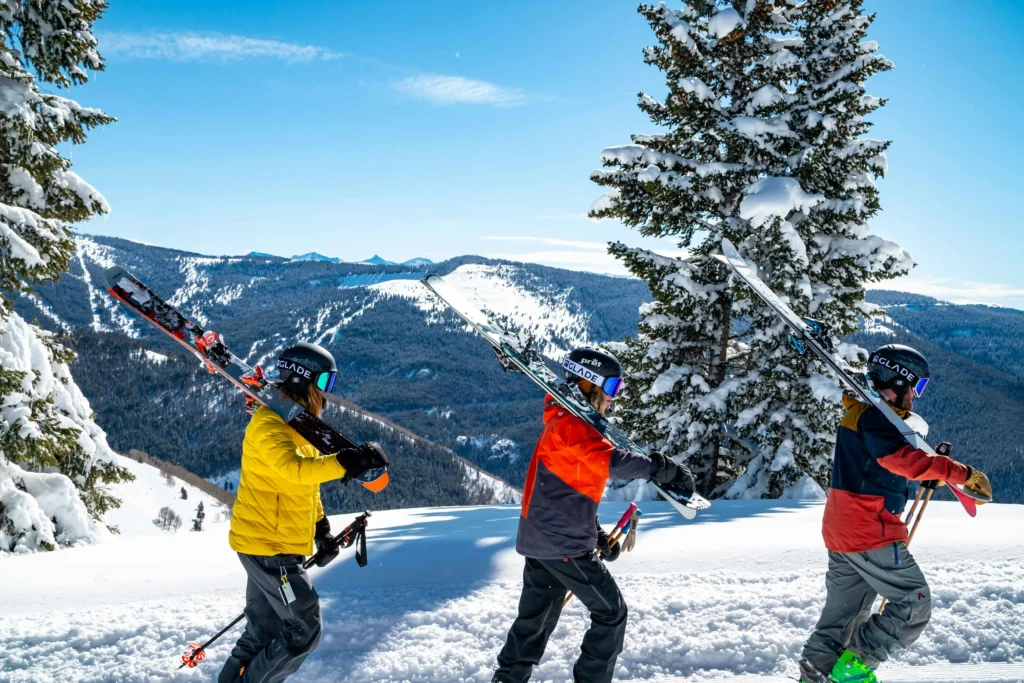 Group of skiers carrying their skis while walking through a snowy mountain landscape on a sunny winter day