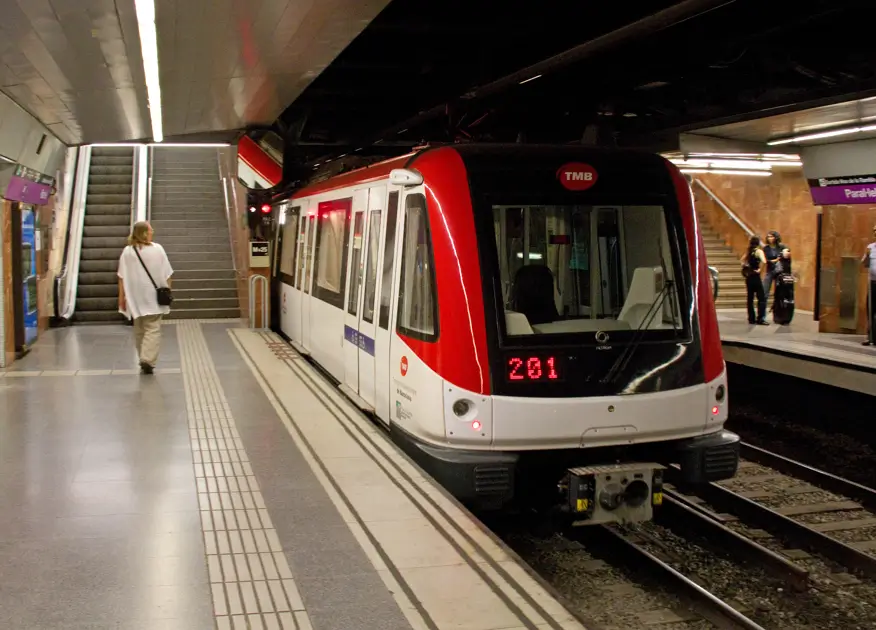TMB metro train stopped at an underground station in Barcelona, with an accessible platform, escalators, and passengers waiting.