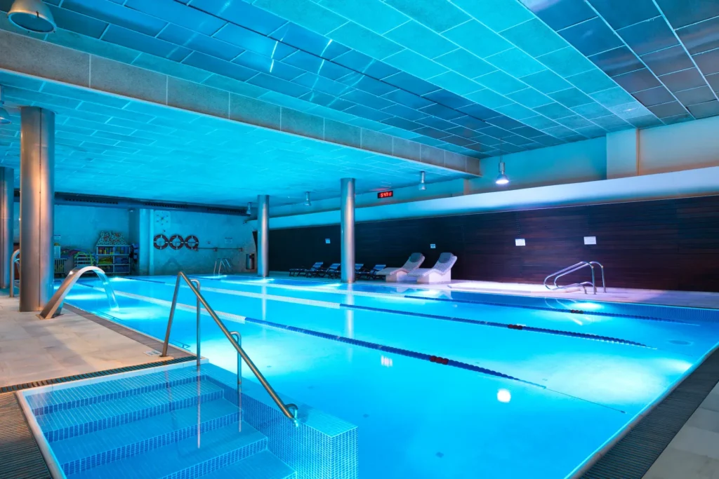 Piscina cubierta climatizada con iluminación azul y zona de descanso, ideal para relajarse y nadar durante todo el año en Barcelona