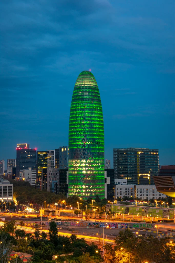 Vista nocturna de la Torre Glòries iluminada en color verde, con el skyline urbano del distrito tecnológico de Barcelona al fondo