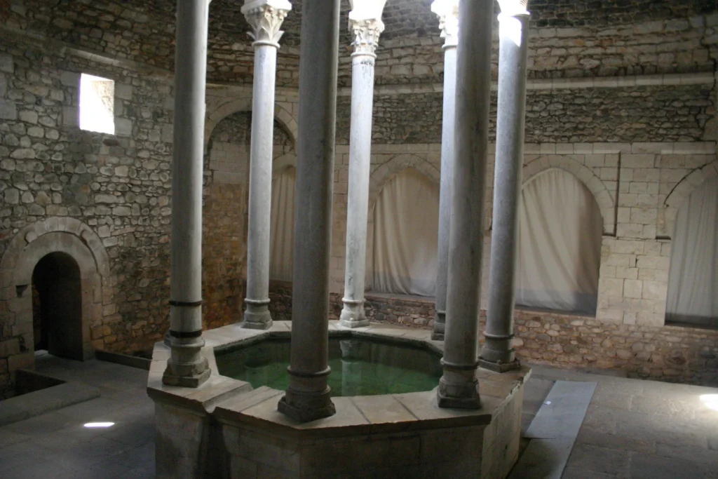 Interior de los Banys Àrabs de Girona con columnas de piedra que rodean una piscina central octogonal bajo una cúpula histórica.