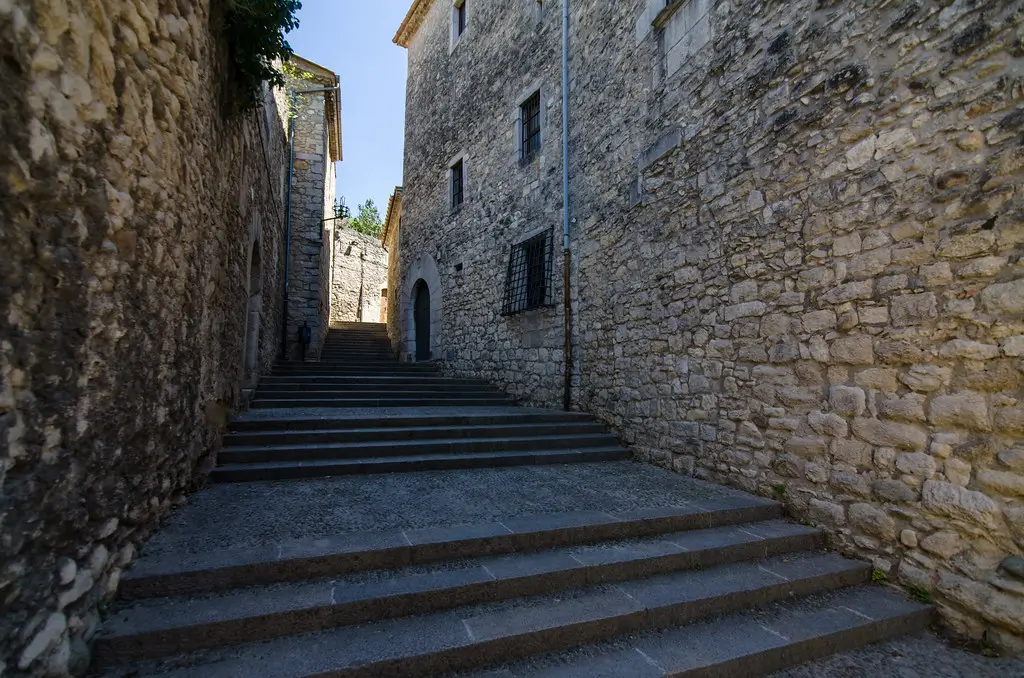 Escaleras de piedra en una estrecha calle del Barri Vell de Girona, rodeadas de edificios históricos de muros de piedra en un entorno tranquilo y soleado.