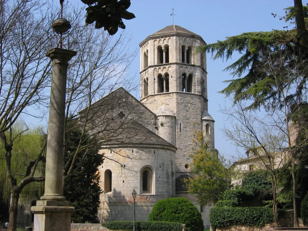 Vista exterior del Monasterio de Sant Pere de Galligants en Girona, con su torre románica y jardines alrededor en un día despejado.