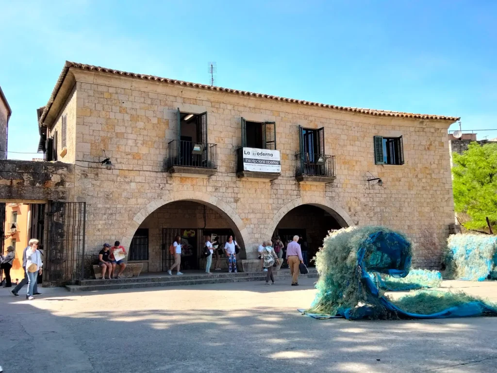 Vista de la Plaça dels Jurats en Girona durante el festival Temps de Flors, con una instalación artística azul en primer plano y la fachada histórica de piedra al fondo.