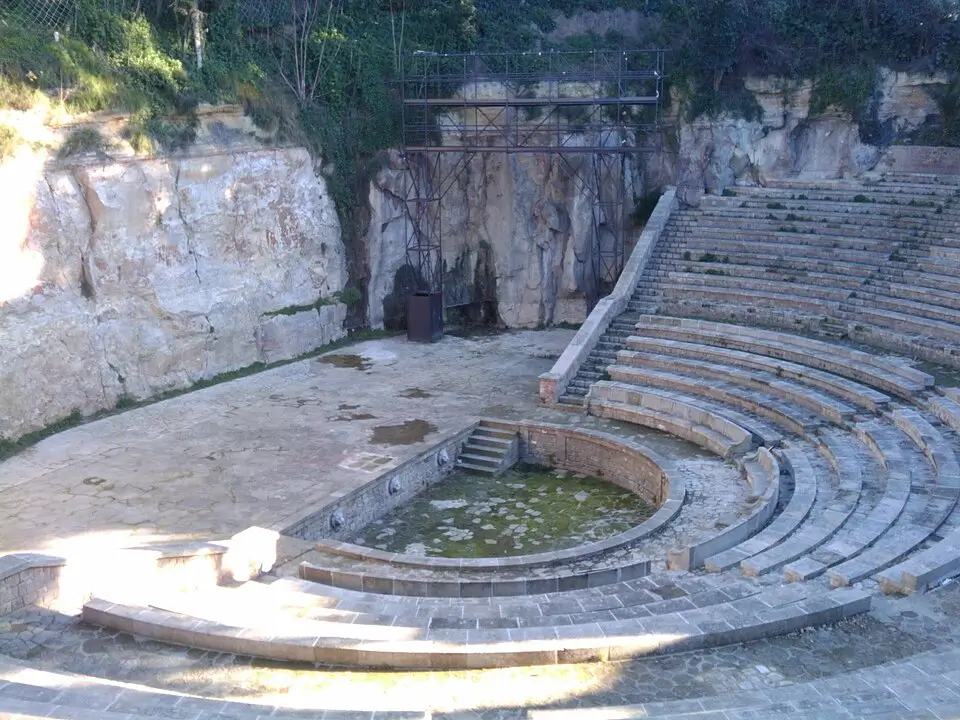 Vue du Teatre Grec de Montjuïc à Barcelone, avec ses gradins en pierre en demi-cercle et sa scène en plein air entourée de roche naturelle et de végétation.