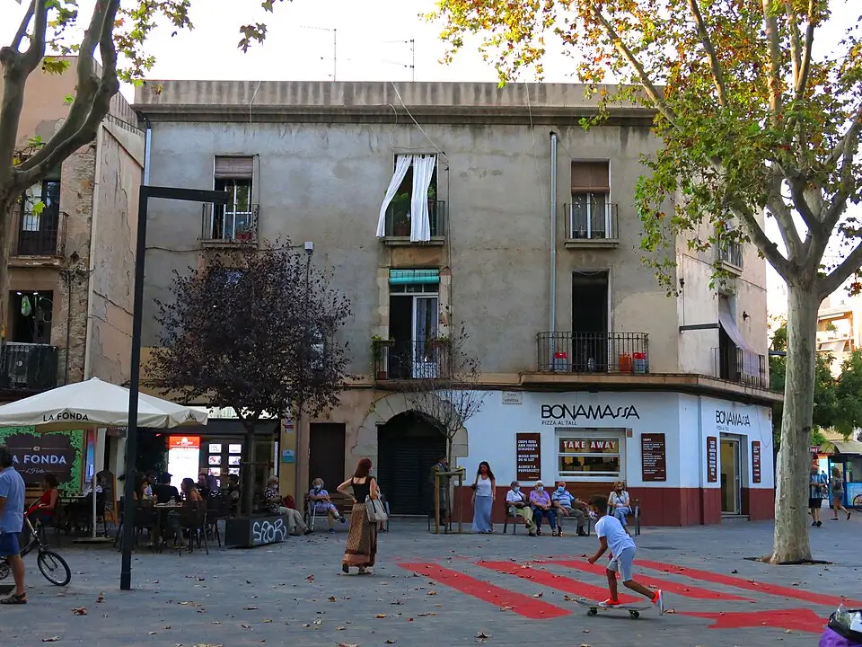 Vista de la Plaça Eivissa en el barrio de Horta, Barcelona, con terrazas, vecinos, comercios locales y ambiente tranquilo de plaza de barrio.