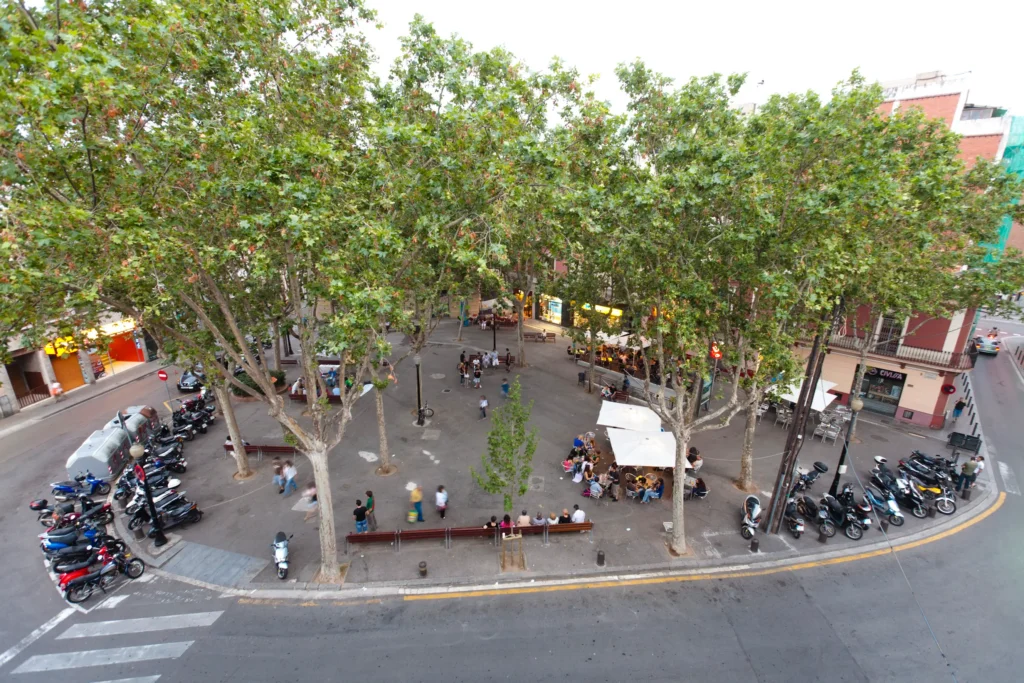 Vista aérea de la Plaça Eivissa en el barrio de Horta-Guinardó, Barcelona, con árboles, terrazas, bancos y ambiente de plaza local.