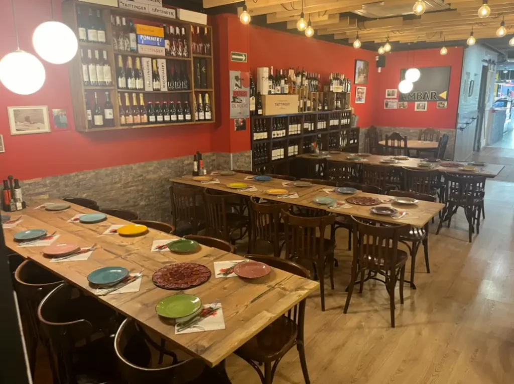 Restaurante acogedor en Barcelona con mesas de madera largas, sillas clásicas y estanterías llenas de botellas de vino en un ambiente cálido y tradicional