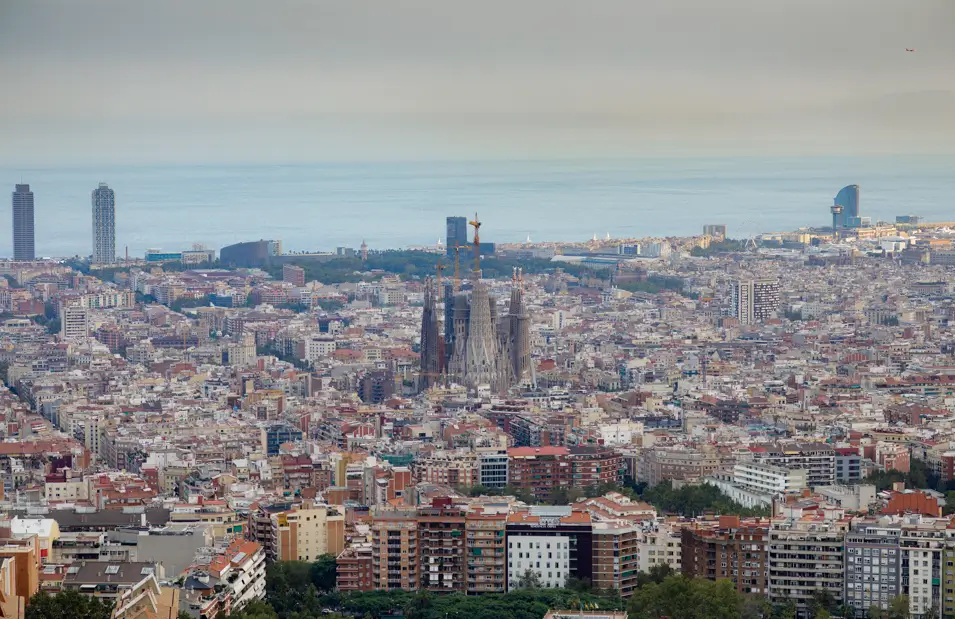Panorámica de Barcelona desde las alturas con la Sagrada Familia en el centro, el mar Mediterráneo y el skyline de la ciudad al fondo.