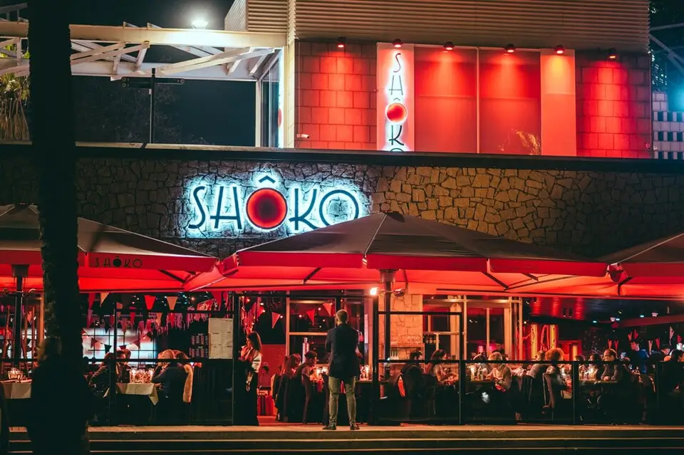 Fachada y terraza del restaurante y discoteca Shôko en Barcelona iluminada en rojo, con personas cenando y ambiente nocturno