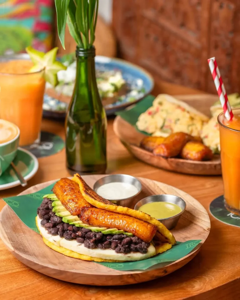 Plato de brunch con plátano caramelizado, aguacate y alubias negras acompañado de zumos naturales y café en una acogedora cafetería de La Barceloneta, Barcelona.