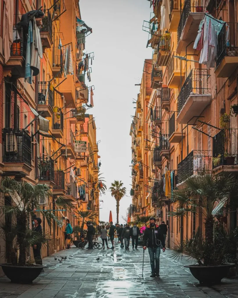 Vista de una calle peatonal de La Barceloneta con edificios históricos, balcones, ropa tendida y vecinos paseando, reflejando el ambiente auténtico y la vida cotidiana de este emblemático barrio marinero de Barcelona.