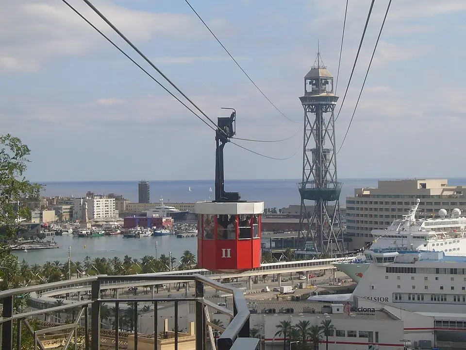 Cabina roja del Teleférico del Puerto de Barcelona con la Torre Jaume I al fondo, vistas al Port Vell, cruceros y el mar Mediterráneo desde la montaña de Montjuïc.