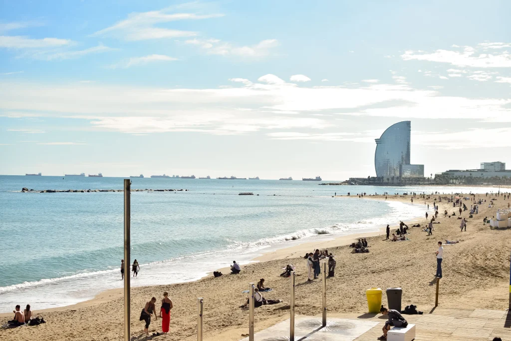 Playa soleada de Barcelona con vistas al mar Mediterráneo y el Hotel W al fondo.