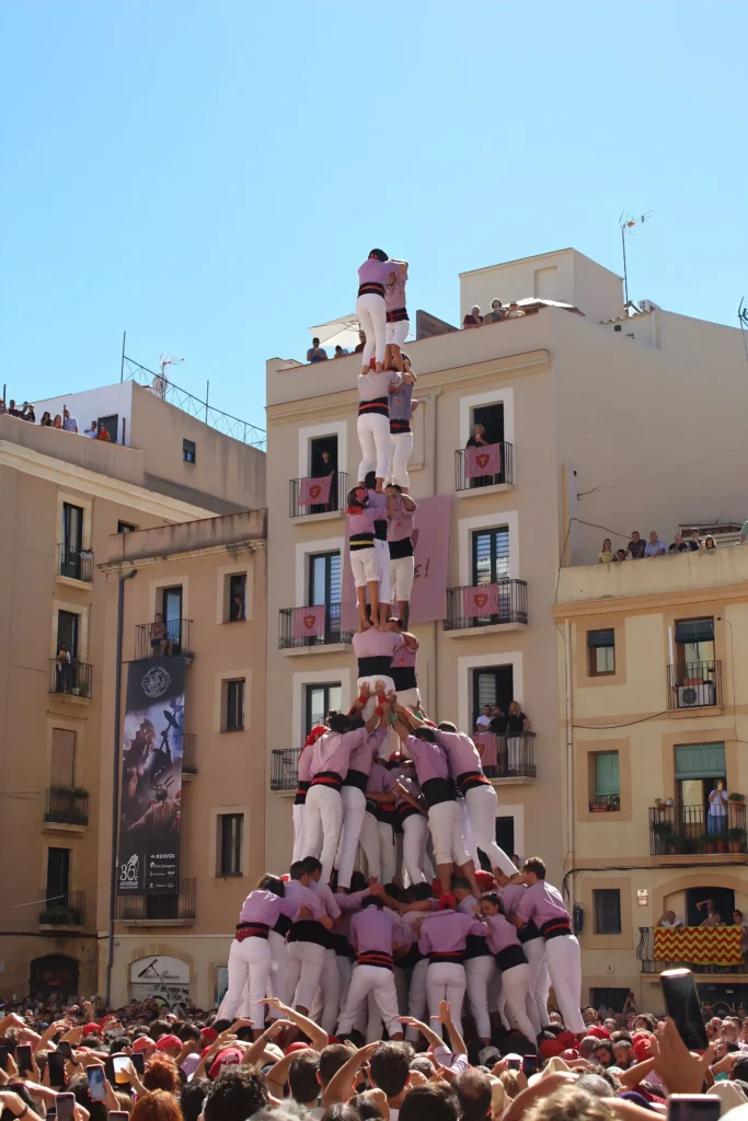 Des castellers construisant une tour humaine traditionnelle lors d'une fête en Catalogne, entourés de nombreux spectateurs.