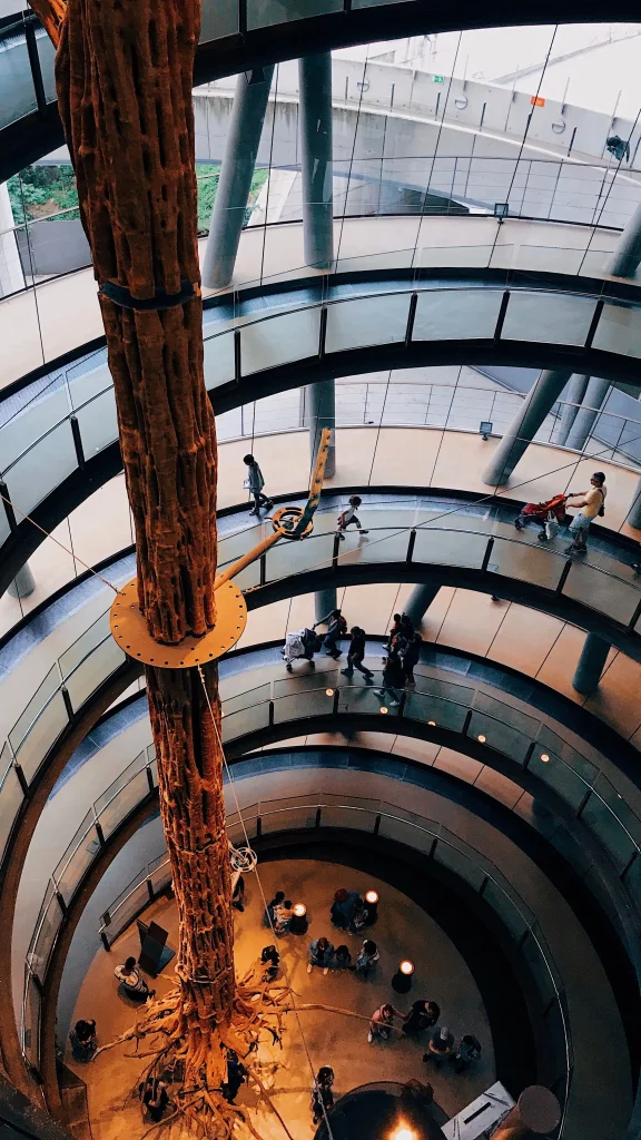 Interno del CosmoCaixa Barcelona con la sua passerella a spirale e un grande albero, mentre alcune famiglie esplorano il museo.