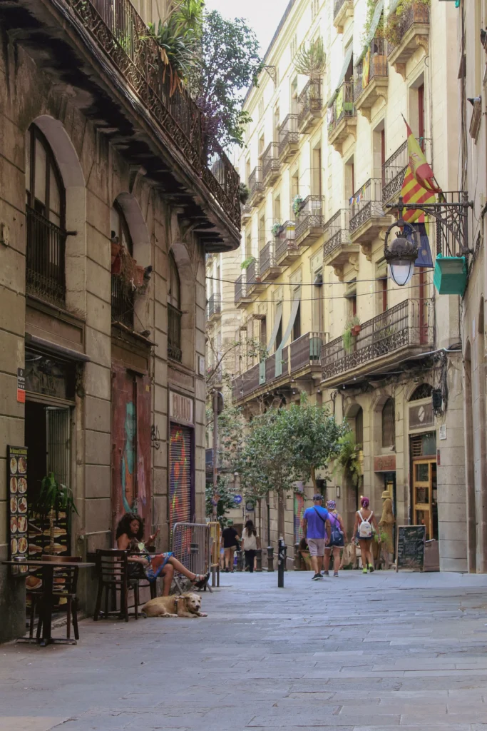 Narrow pedestrian street lined with historic buildings, balconies, small businesses and outdoor seating in Barcelona.