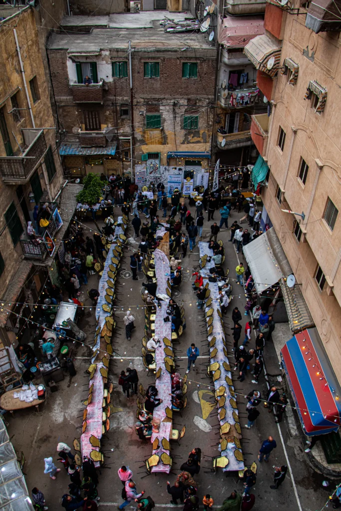 Des habitants réunis autour de longues tables lors d'un repas convivial pendant une fête traditionnelle dans les rues d'un quartier résidentiel.