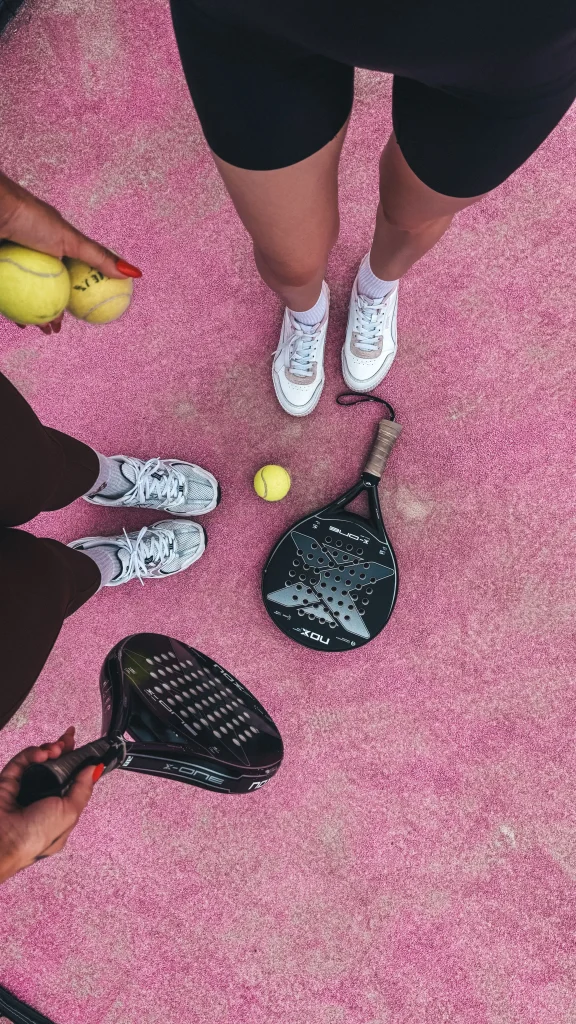 Jugadores de pádel con palas y pelotas juntos en una pista rosa antes de un partido.