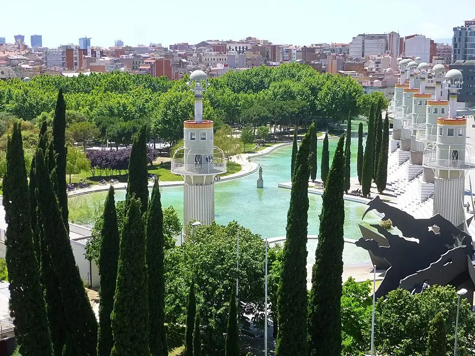 Vue du Parc de l’Espanya Industrial à Barcelone, avec son lac, ses grands cyprès, ses tours caractéristiques et le paysage urbain environnant.