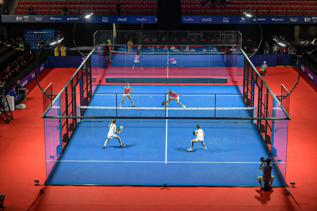Cuatro jugadores disputando un partido profesional de pádel en una pista azul cubierta.