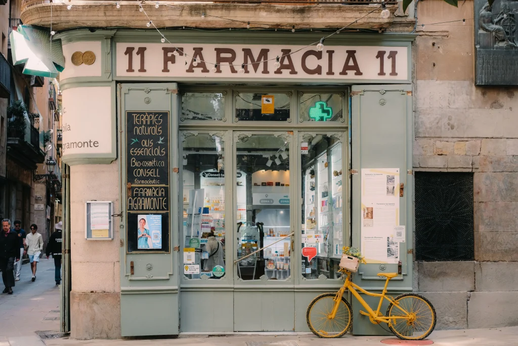 Traditional pharmacy storefront in Barcelona's Gothic Quarter, featuring a historic façade and a yellow bicycle outside.