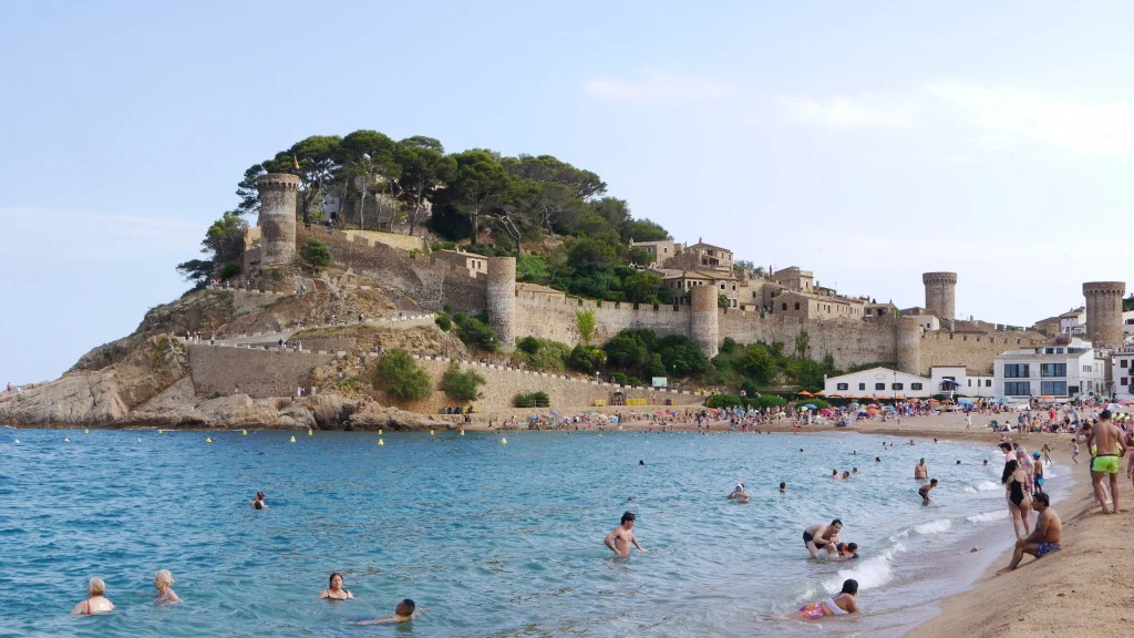 Blick auf den Strand von Tossa de Mar mit den mittelalterlichen Mauern und Türmen der Vila Vella über dem Mittelmeer.