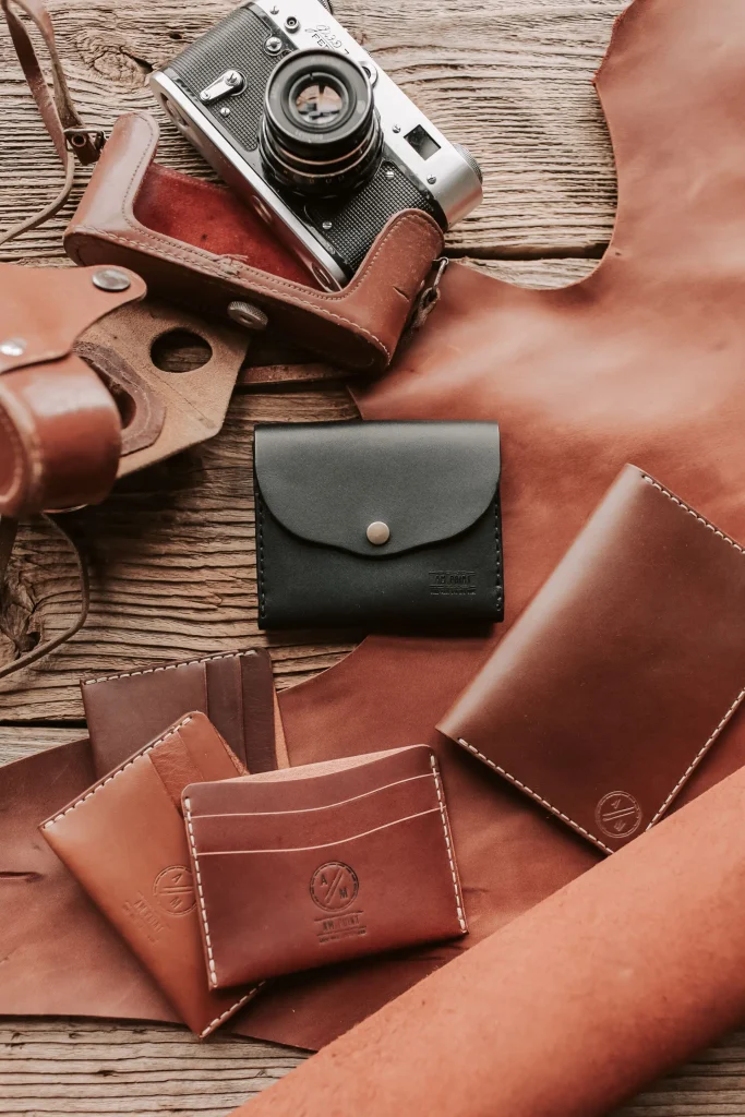 Handcrafted leather wallets and accessories displayed alongside a vintage camera on a wooden surface.