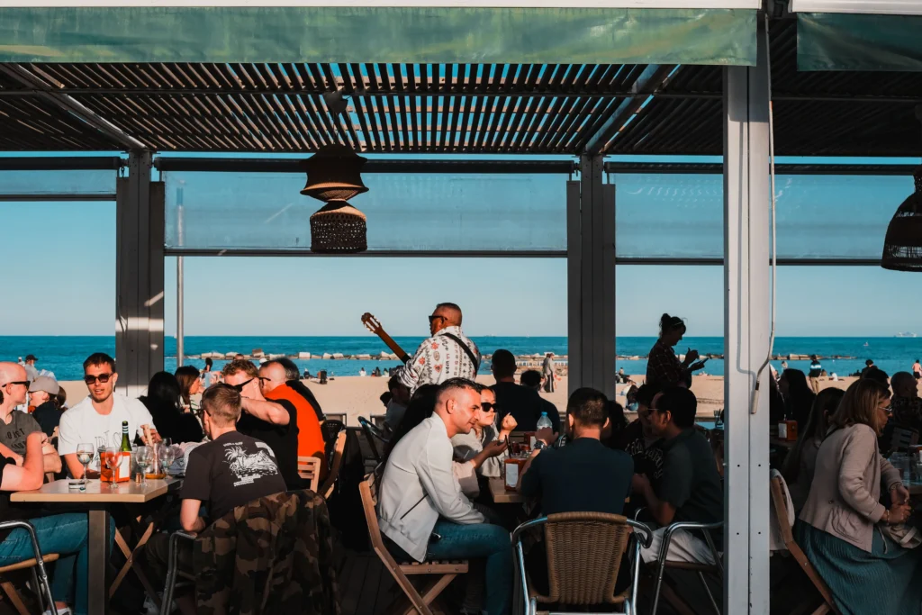 Personas disfrutando de bebidas y música en directo en un bar frente a la playa con vistas al Mediterráneo en Barcelona.