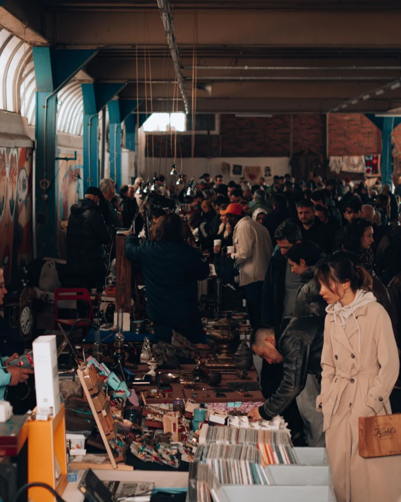 Visitantes observando objetos vintage, discos y artículos de segunda mano en un concurrido mercadillo de Barcelona.